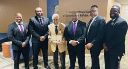 Governor Wilder receives his 75th service medallion and certificate from Omega Psi Phi. Fraternity, Inc. Standing are six men with Governor Wilder in the middle