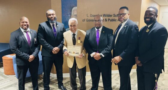 Governor Wilder receives his 75th service medallion and certificate from Omega Psi Phi. Fraternity, Inc. Standing are six men with Governor Wilder in the middle